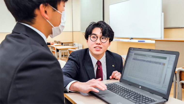 パソコンを使い生徒と成績を見る山本さんの写真